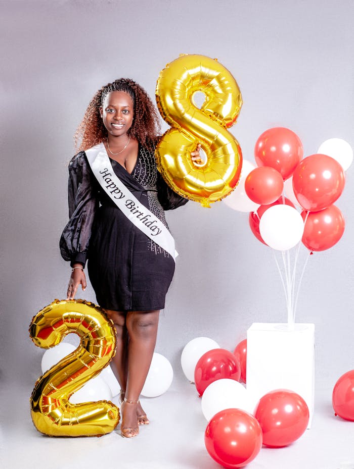 services-10 A woman celebrates her 28th birthday with balloons and a sash indoors.